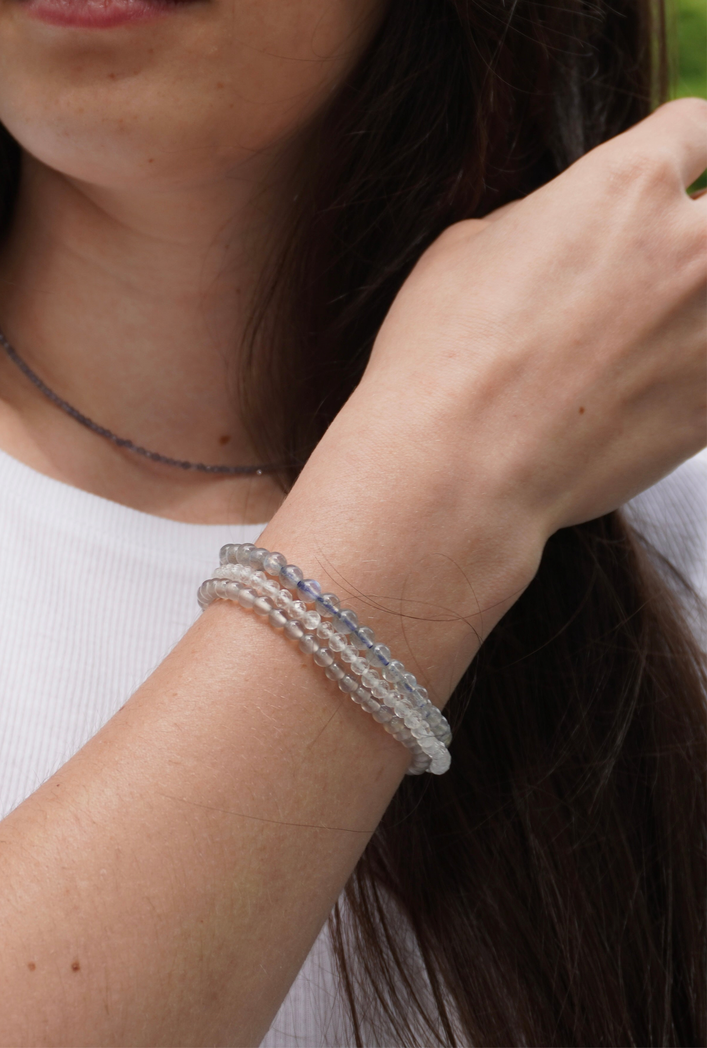 Nahaufnahme eines weiblichen Handgelenks mit drei schimmernden Edelsteinarmbändern aus Achat, Bergkristall und Labradorit – elegant kombiniert und getragen zu einem weißen Shirt, symbolisch für Klarheit, Schutz und Erdung.