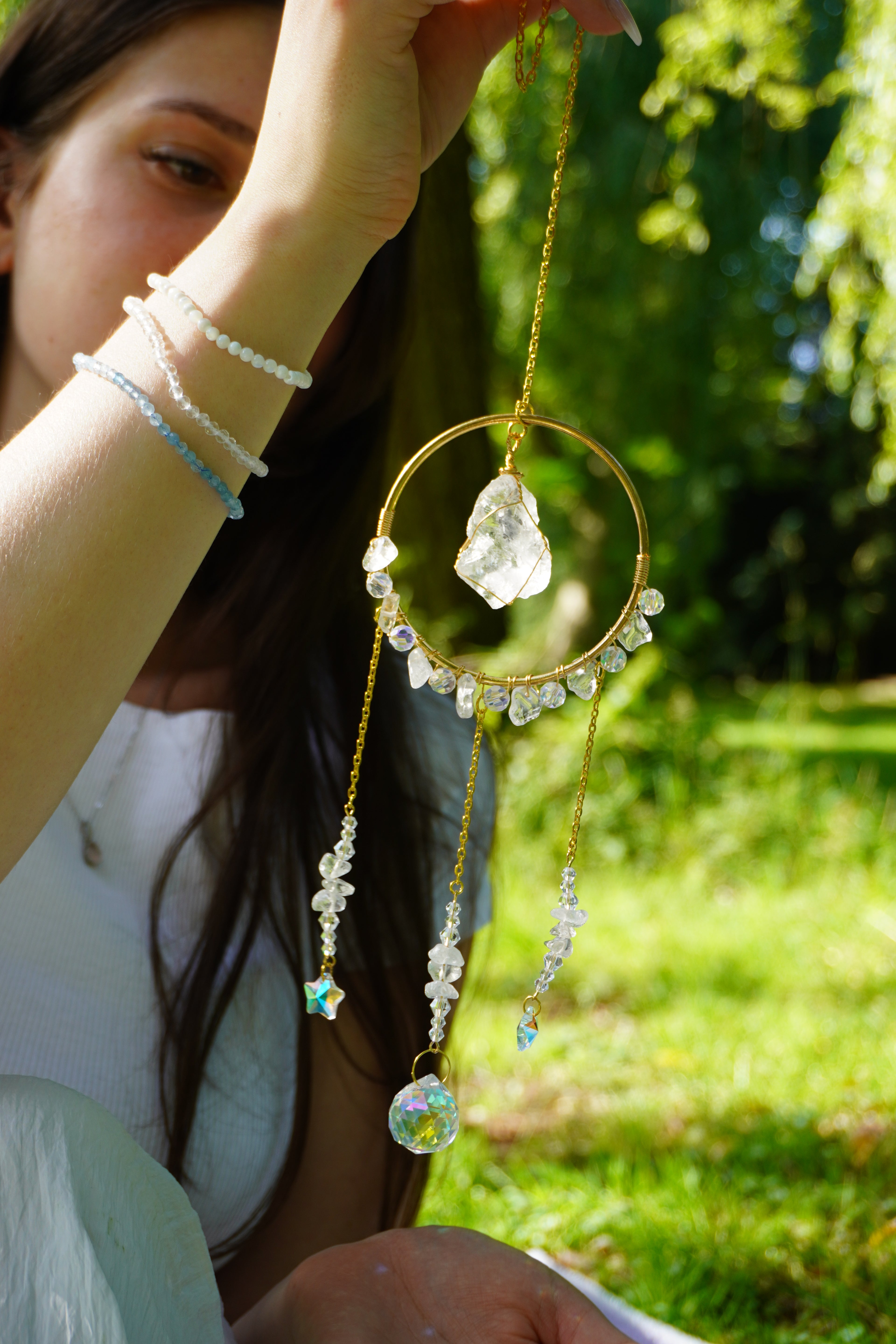 Frau hält einen Sonnenfänger aus Bergkristall in der Sonne – verziert mit goldener Kette und funkelnden Kristallen, eingefangen im natürlichen Licht.