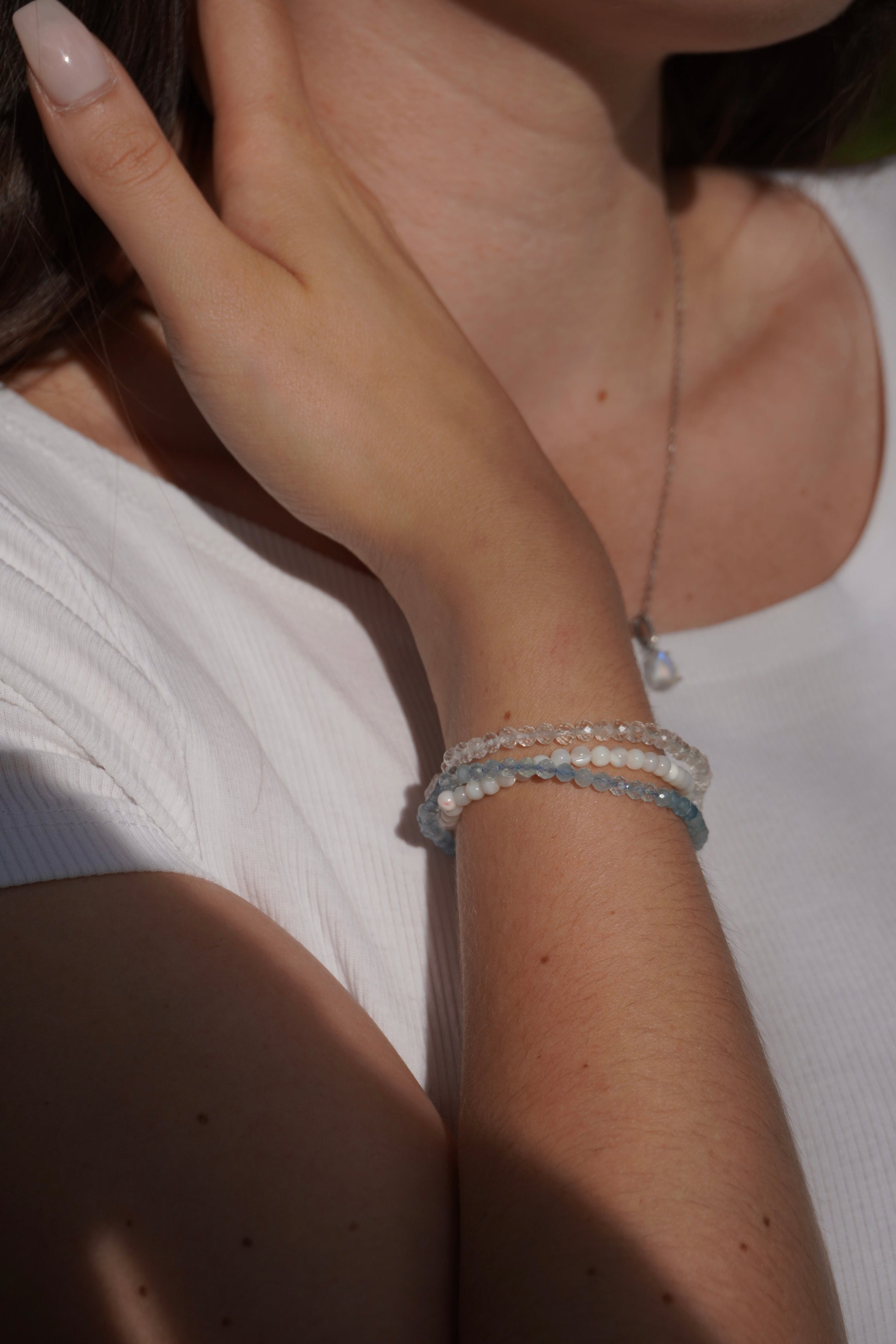 Zarte Edelsteinarmbänder aus Bergkristall, Aquamarin und Perlmutt an einem weiblichen Handgelenk. Für Klarheit, innere Ruhe und Selbstliebe.