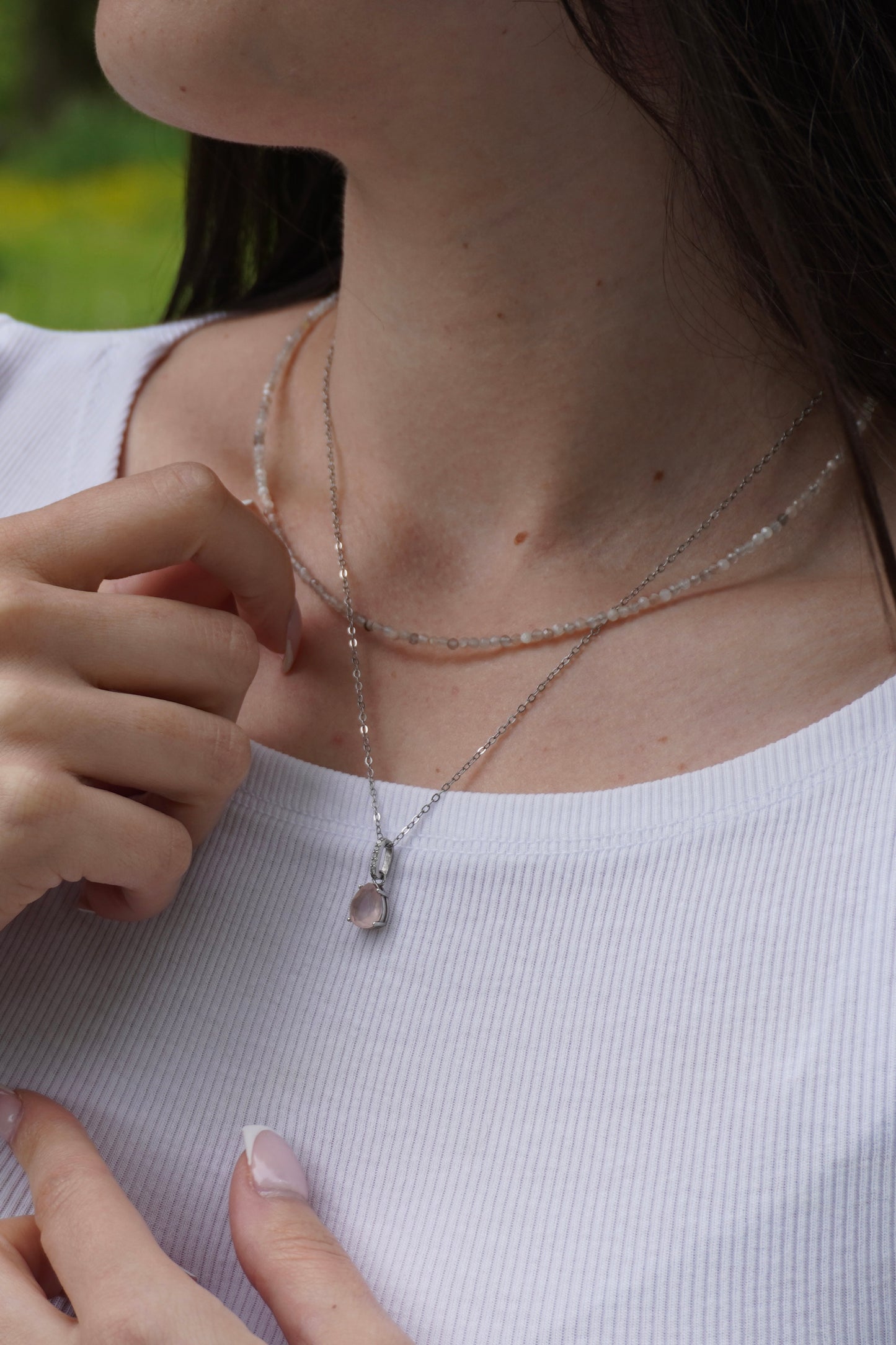 Zarte Halskette aus facettiertem Mondstein und silberne Kette mit Tropfenanhänger aus Rosenquarz – getragen an weiblichem Hals