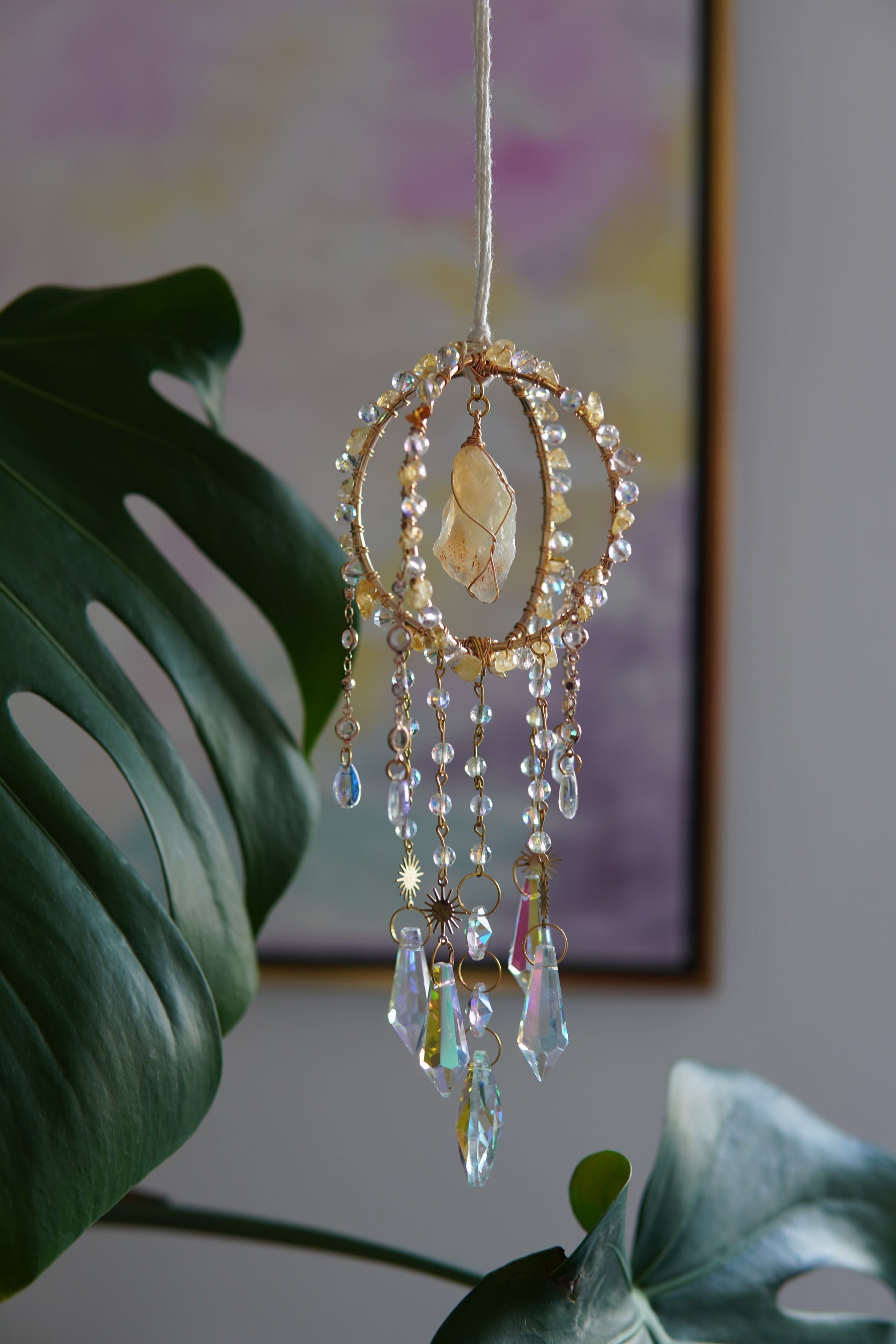 Handgemachter Sonnenfänger mit goldfarbenem Ring und schimmernden Kristallen – spirituelle Fensterdeko aus Edelsteinen, ideal als Geschenkidee bei Sonnenlicht und Pflanzen.