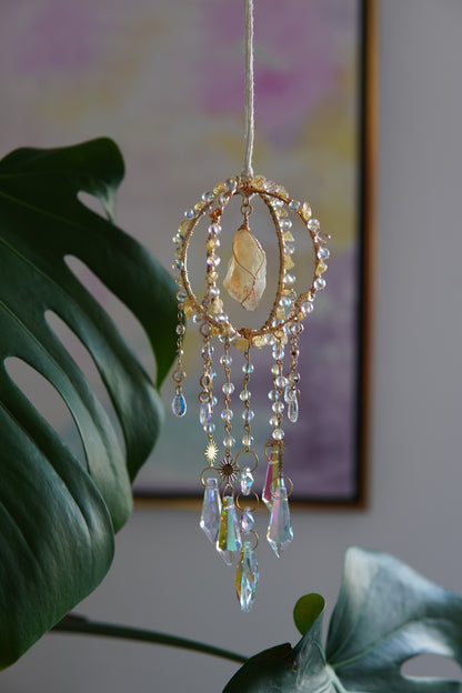 Handgemachter Sonnenfänger mit goldfarbenem Ring und schimmernden Kristallen – spirituelle Fensterdeko aus Edelsteinen, ideal als Geschenkidee bei Sonnenlicht und Pflanzen.
