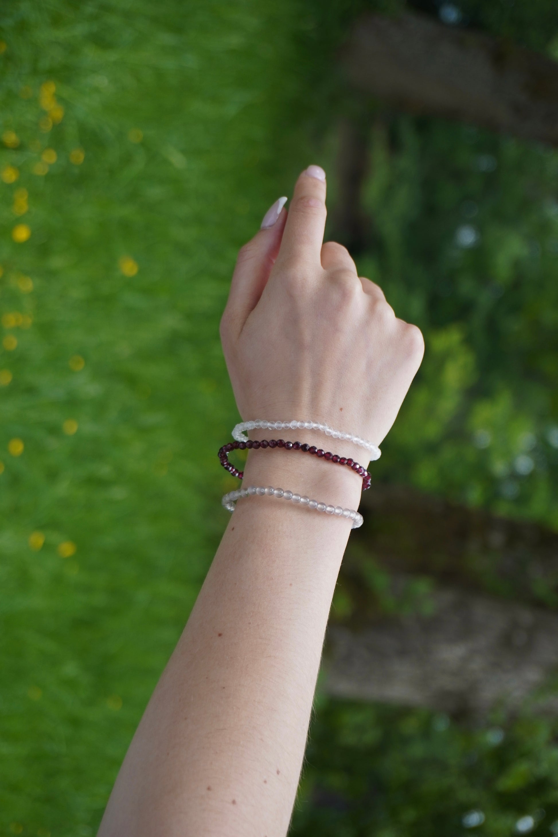 Arm einer Frau mit Armbändern aus facettiertem Granat, Bergkristall und Achat– aufgenommen in natürlicher Umgebung, Symbol für Stärke, Klarheit und Erdung.